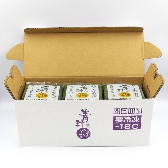 開いた段ボール箱の中に、日本語の文字が書かれた緑色の青汁のパッケージが 3 つ入っています。箱には -18°C での保管要件が記載されています。