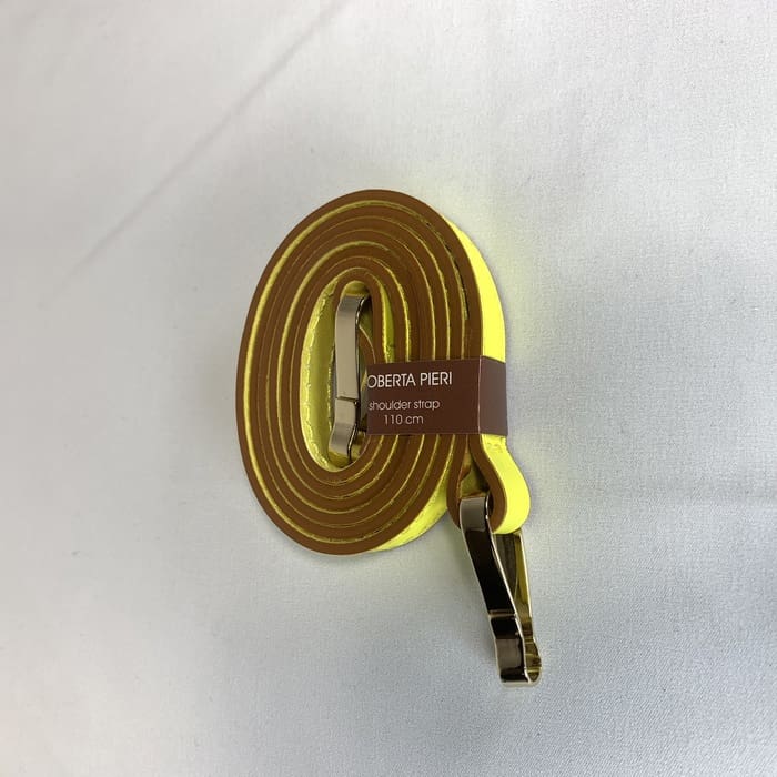 A alça de ombro amarela com acessórios dourados é enrolada e a etiqueta marrom "ROBERTA PIERI shoulder strap 110 cm" é adornada na superfície branca.