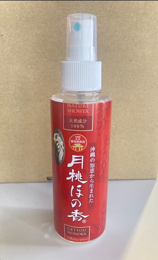 Um frasco de spray vermelho com as palavras "Nature Shower" escritas em um fundo bege. Bico de pulverização e tampa brancos.
